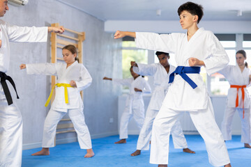 Determined boy in white kimono practicing punches in gym during martial arts workout with...