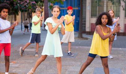 Obraz premium Confident positive preteen boys and girls dancing modern choreography on city street on sunny summer day..