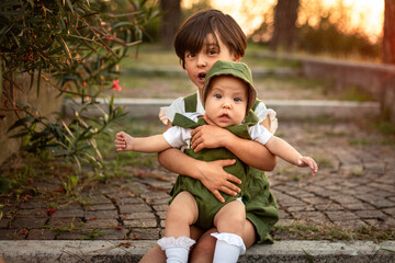 portrait of two sitting children, bigger one holding smaller one in hands