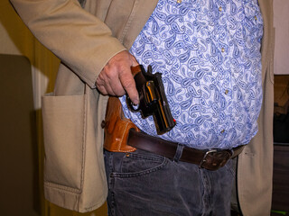 A man holding a black revolver drawn from his holster.