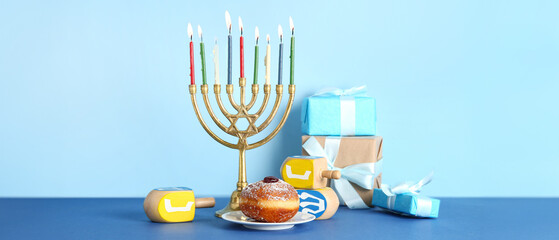 Menorah with gift boxes, tasty donut and dreidels on color background. Hanukkah celebration