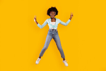 Joy Of Success. Bushy Black Millennial Woman Jumping Gesturing Victory V-Sign With Both Hands Posing In Mid-Air Over Pink Studio Background. Young Female Jumps Expressing Positive Emotions. Vertical