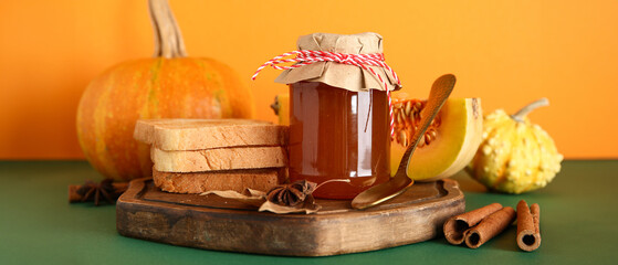 Jar of sweet pumpkin jam with different spices and toasts on colorful background