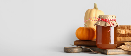 Wooden board with jar of sweet pumpkin jam and toasts on white background