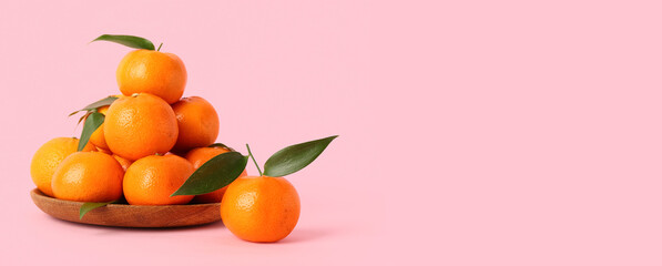 Wooden plate with sweet mandarins on pink background