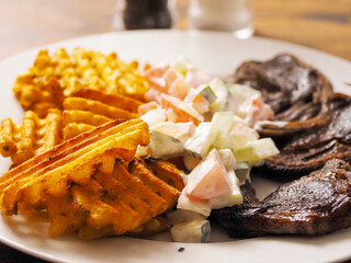 Dinner with well cooked lamb chops on the bone, potato lattice shape chips and fresh salad with cream. High quality products. Tasty properly meal. Fine simple food.