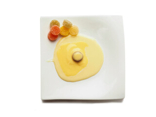 Condensed milk and custard desert looks like a fired egg and colorful jelly sweets in sugar on a white fancy square plate and light background. Creative food ideas. Light and airy look