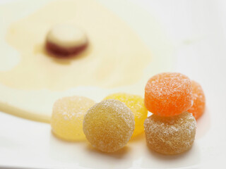 Condensed milk and custard desert looks like a fired egg and colorful jelly sweets in sugar on a white fancy square plate and light background. Creative food ideas. Light and airy look