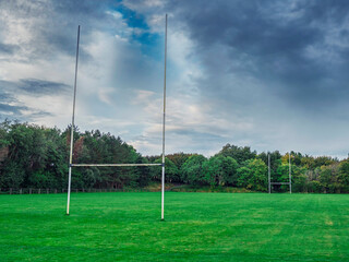 Training grass field with tall goalposts for Irish national games like rugby, hurling, Gaelic football and camogie, Beautiful cloudy sky. Nobody. Sport area in a park. Rich green tones.