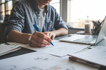 Checkered shirted person sketches at desk, creating a focused, creative work environment.