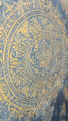 An intricate golden ornamental design embossed on a textured gray surface, featuring floral and geometric patterns. Ideal for luxury design concepts, wallpaper, or decor-related projects.