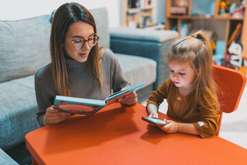 A serene moment captures a woman immersed in reading while a young girl engrossed in using a...
