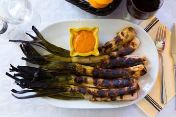 Top view of grilled calcots traditionally served with romesco sauce and red wine in restaurant. National Catalan winter dish