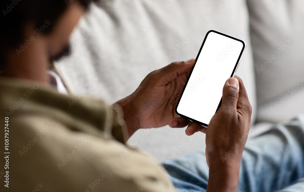 Poster unrecognizable black male using smartphone with blank white screen at home, over shoulder view of af