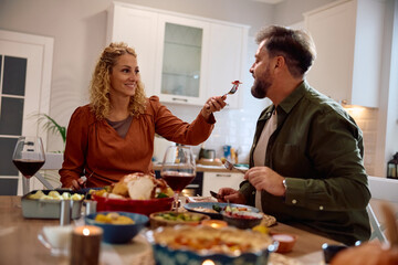 Happy woman eating with her husband in dining room on Thanksgiving.
