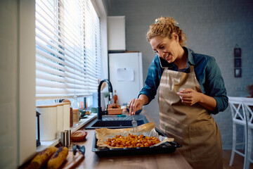 Happy woman talking on cell phone while preparing food in kitchen.