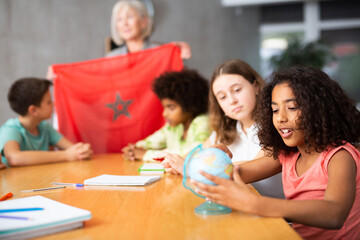Attentive ten-year-old schoolgirl is studying the history of Marroko in lesson and is looking for her on the globe