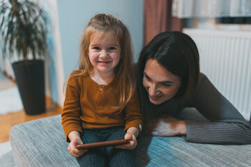 A child smiles warmly while using a smartphone with a parent nearby, capturing a loving family interaction with technology in a comfortable indoor setting.