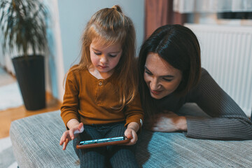 A young child attentively uses a smartphone while an adult supervises, showcasing modern technology...