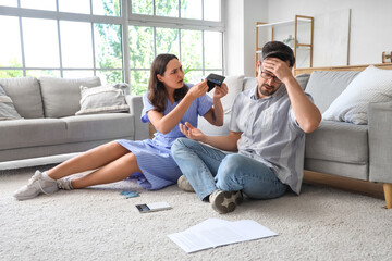 Obraz premium Young couple sitting on floor with empty wallet and arguing at home. Bankruptcy concept