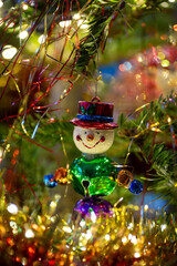 Festive snowman clown Christmas tree ornament with bells. Festive decoration with gold and red lametta, tinsel and fairy lights.