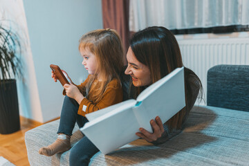A touching scene where a mother indulges in reading while her child engages with a smartphone,...