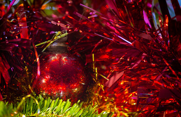 Red festive bauble with cracked mirror surface on Christmas tree with red tinsel.