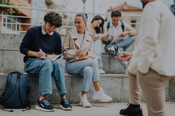 Group of high school students sitting outdoors, collaborating on tasks with the help of a...