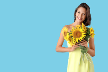 Beautiful young happy woman with bouquet of sunflowers on blue background