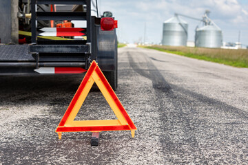 Work trailer on side of road with warning triangle. Emergency roadside assistance, work zone, and towing safety concept.