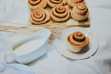 Fresh cinnabons on a wooden tray along with milk on a white fabric background