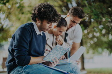 A group of university students collaborate while studying in a park. They engage in discussion and take notes, reflecting teamwork and academic dedication in a relaxed outdoor setting.