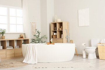 Bathtub with towel, toilet bowl and shelving units in interior of bathroom