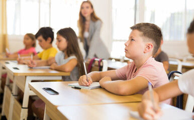 Portrait of focused preteen schoolboy writing exercises in workbook during lesson in classroom ..