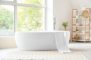 Bathtub with towel and shelving unit in interior of bathroom