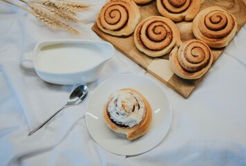 Fresh cinnabon on a plate on a background of other buns on a wooden tray and milk with a spoon