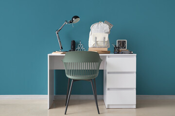 Stylish children's workplace with lamp, clock and school bag near blue wall in room