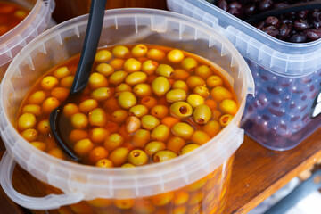 Pile of large green pitted olives lies in bucket in greengrocer's shop..