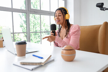 Young African-American woman with headphones and microphone recording podcast in studio