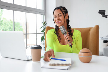 Young African-American woman with microphone recording podcast in studio