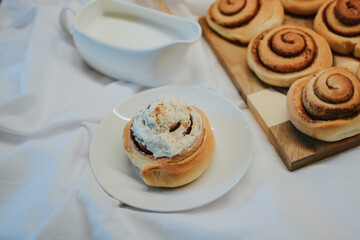 Fresh cinnabon on a plate on a background of other buns on a wooden tray and milk with a spoon