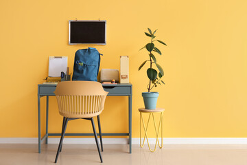 Workspace with school supplies, blank chalkboard and backpack near yellow wall