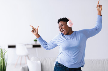 Enjoying Favorite Song. Emotional excited curvy black woman wearing wireless headset listening to...