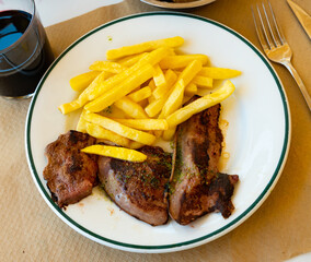 Few pieces of lamb liver are garnished with portion of French fries. Liver is cooked with parsley and garlic, spicy seasoning. Dish is served with red wine and white baguette.