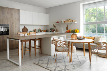 Plates in shape of pumpkin, berries and autumn flowers on table in light kitchen