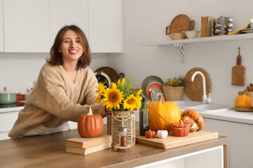 Pretty young woman with autumn flowers, pumpkins and books in light kitchen