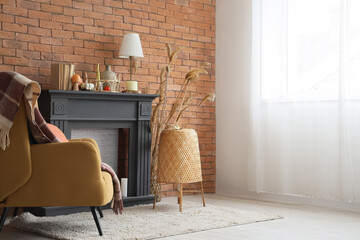 Fireplace, soft armchair with plaid, lamp and pampas grass in autumn living room