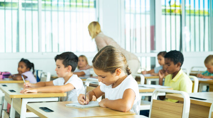 Portrait of focused tween schoolgirl writing exercises in workbook in classroom during lesson