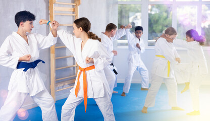 Boy and girl in kimono practicing karate techniques in group in studio..