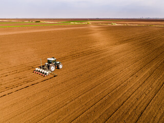 Obraz premium Tractor seeding crops in plowed field, agriculture industry